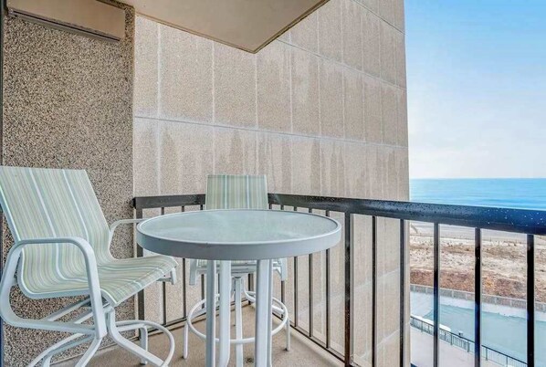 A balcony with a round table and two striped chairs, a view of the beach, and a tiled wall. - Sea Colony Ocean 6th floor condo w/ shared sauna, elevator, and free WiFi (Bethany Beach)
