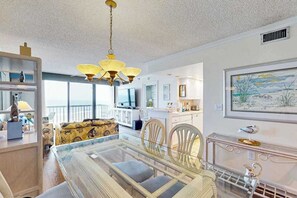 A modern living room with a glass dining table, a yellow sofa, and a chandelier. - Sea Colony oceanfront condo with pools, hot tub, sauna, balcony & pickleball (Bethany Beach)
