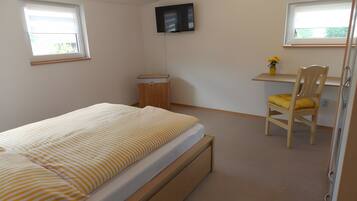 Een slaapkamer met een bed, een bureau, een stoel, een televisie en een raam.