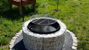 A circular outdoor grill with a metal grate, surrounded by a stone wall, set in a grassy area.