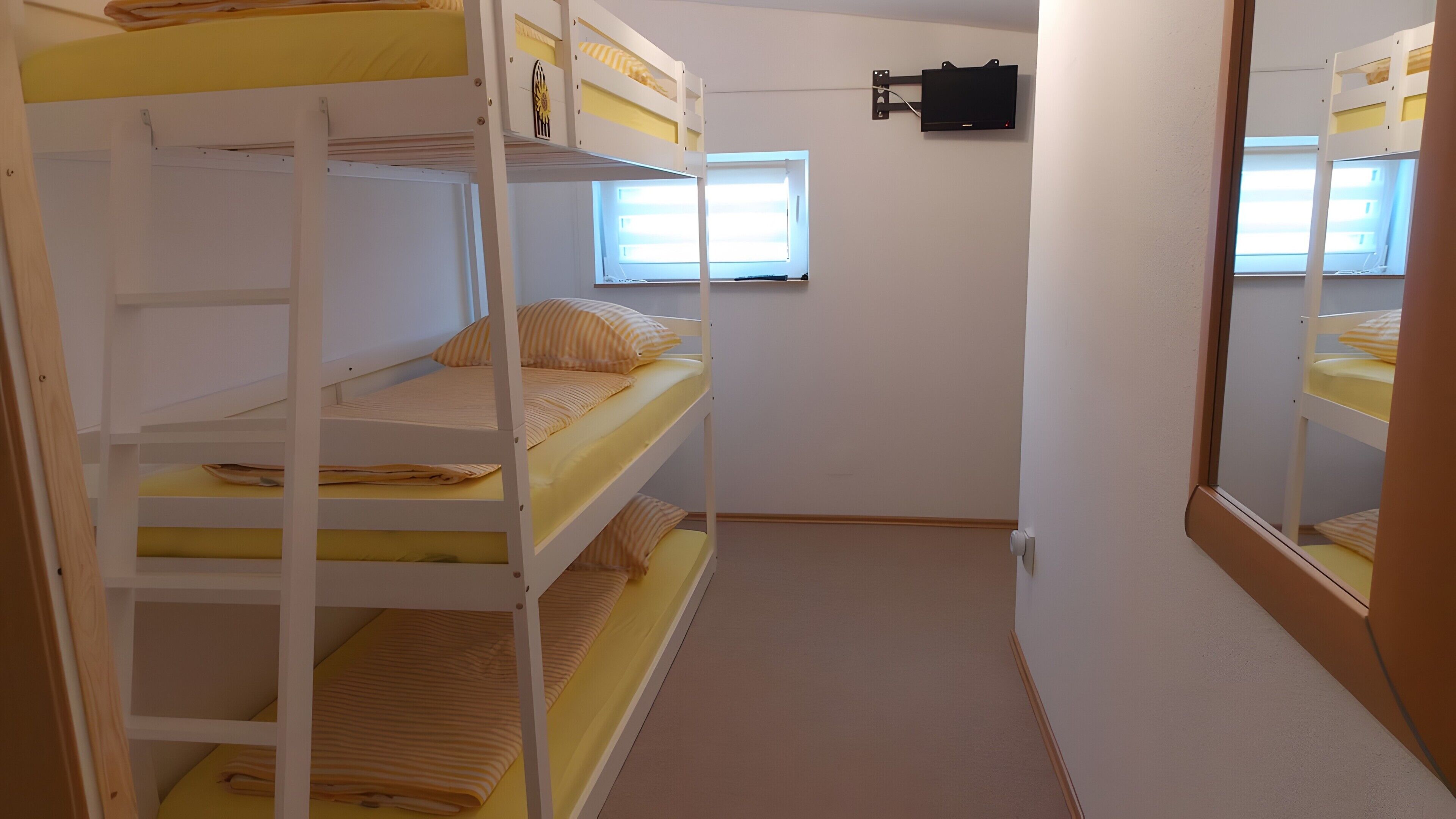 Une chambre avec un lit superposé, une fenêtre, un téléviseur fixé au mur et une porte.