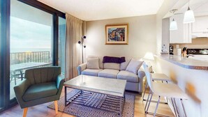 Una camera d'albergo moderna con un balcone, un divano, un tavolino da caffè e un angolo cottura.