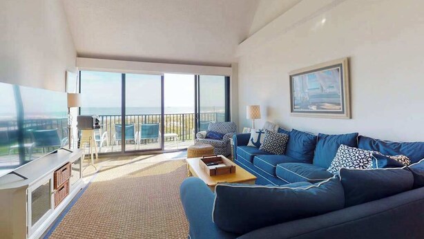 Ein modernes Wohnzimmer mit einem blauen Sofa, einem Flachbildfernseher und einem Balkon mit Blick.