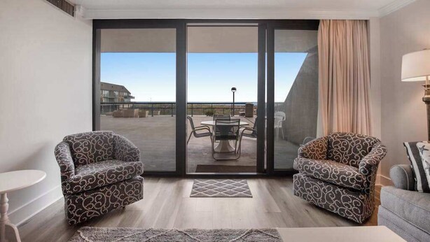 Een kamer met twee gestoffeerde fauteuils, een bank, een tafel en uitzicht door een grote schuifdeur op een terras.
