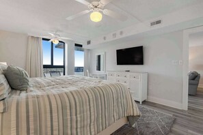 Ein Schlafzimmer mit Bett, Deckenventilator, Fernseher, Kommode und Blick ins Freie.