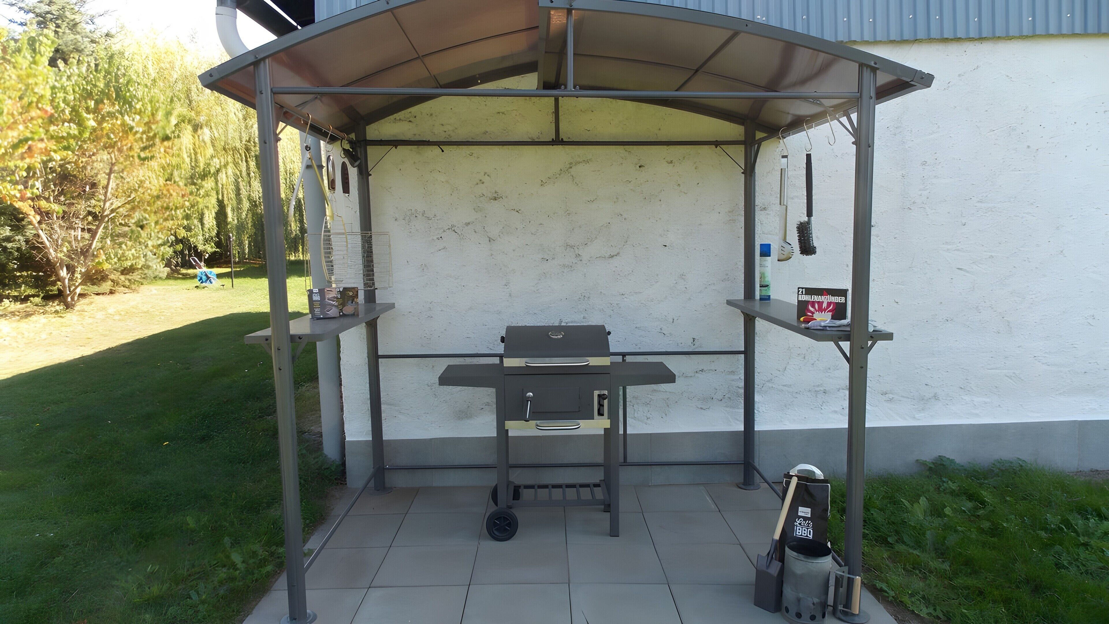 A covered outdoor barbecue area with a grill, a cart, and a bag labeled 'BBQ.'