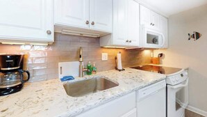 A kitchen with white cabinets, a stainless steel sink, a coffee maker, and a microwave. - Sea Colony Ocean 5th floor condo w/ tennis court, pool, and elevator (Bethany Beach)
