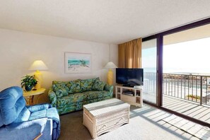 Ein Wohnzimmer mit Sofa, Fernseher, Lampe und einem Balkon mit Blick.