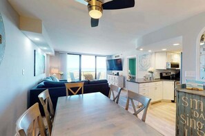 A modern living space with a dining area, kitchen, and a balcony with a view. - Sea Colony Ocean 2nd floor condo w/ shared sauna, gym, and pool (Bethany Beach)