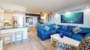 Ein modernes Wohnzimmer mit blauem Sofa, einer Küchenzeile und einem Essbereich.
