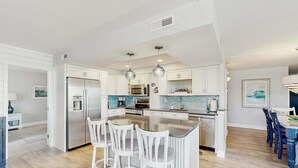 Uma cozinha moderna com armários brancos, eletrodomésticos de aço inoxidável e uma ilha central com banquetas.