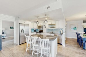 A modern kitchen with white cabinetry, stainless steel appliances, a central island with bar stools, and pendant lighting. - Sea Colony Ocean 2nd floor condo w/ elevator, gym, and free WiFi (Bethany Beach)
