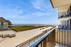 Un balcón de hotel con vista a la playa, mobiliario exterior y una barandilla.