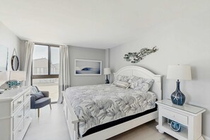 Un dormitorio con cama, mesitas de noche, cómoda, una silla y ventana con cortinas.