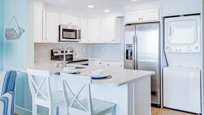 Una cocina moderna con armarios blancos, una isla central, electrodomésticos de acero inoxidable y una lámpara colgante.
