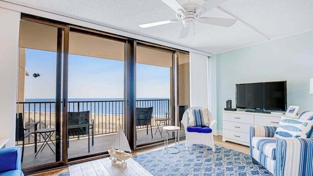 Un balcón con vista a la playa, ventilador de techo, televisor y sofá.