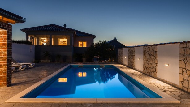 Une piscine avec un mur en pierre et une maison en arrière-plan.