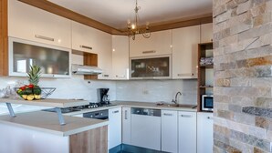 Une cuisine moderne avec des meubles blancs, une cuisinière encastrée et un mur d’accent en pierre.