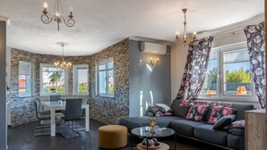 Un salon moderne avec un mur en pierre, un coin repas doté d’une table en verre et un canapé agrémenté de coussins à motifs floraux.