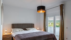 Une chambre à coucher avec un lit, des tables de chevet, un luminaire suspendu et une vue par la fenêtre.