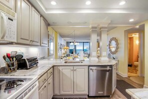 A modern kitchen with a built-in dishwasher, a large island with a sink, and a view to the living area. - Sea Colony Ocean 6th floor condo w/ pool, gym, and free WiFi (Bethany Beach)