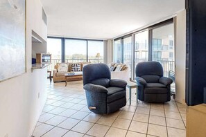 Un salón moderno con dos sillones oscuros, un sofá y un ventanal con vistas a la ciudad.