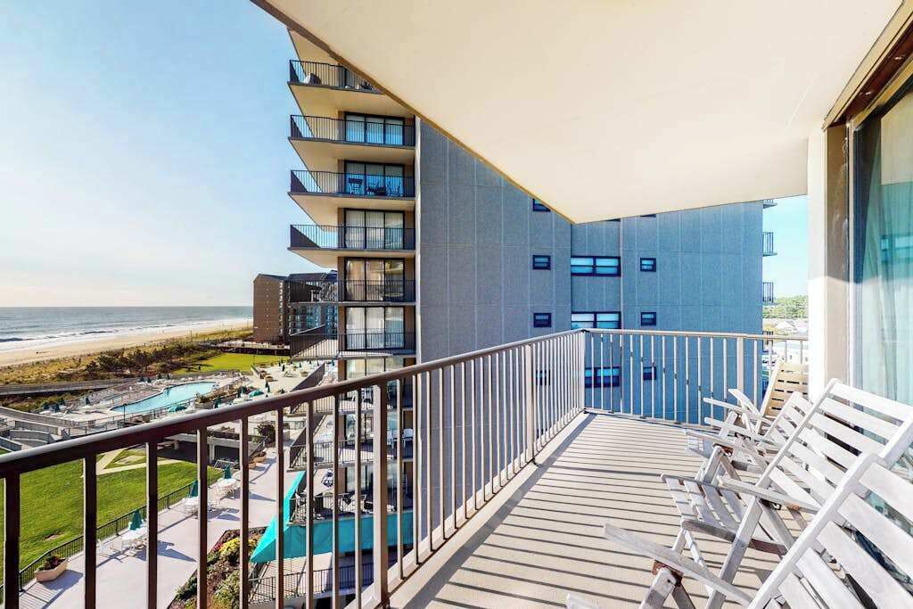 Een balkon met uitzicht op het strand en zwembad, een modern gebouw met balkons en ligbedden.