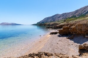 Paisagem costeira com água cristalina, costa rochosa e montanhas ao longe.