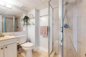 Une salle de bain comprenant des toilettes, un lavabo, un miroir, une douche en verre et un porte-serviettes.