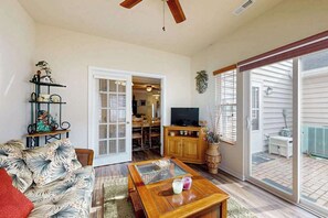 Ein Wohnzimmer mit einer Couch, einem Couchtisch, einem Fernseher und einer Schiebetür zu einer Terrasse.
