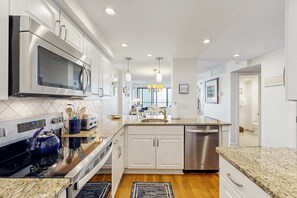 Een moderne keuken met roestvrijstalen apparatuur, witte kasten, granieten aanrecht en een centraal eiland met een spoelbak.