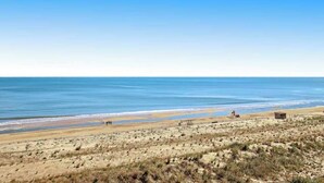 Une plage avec un ciel dégagé, des dunes de sable et une petite construction visible au loin.