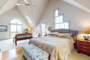 Un dormitorio con una cama grande, un banco, un ventilador de techo y vistas al exterior.
