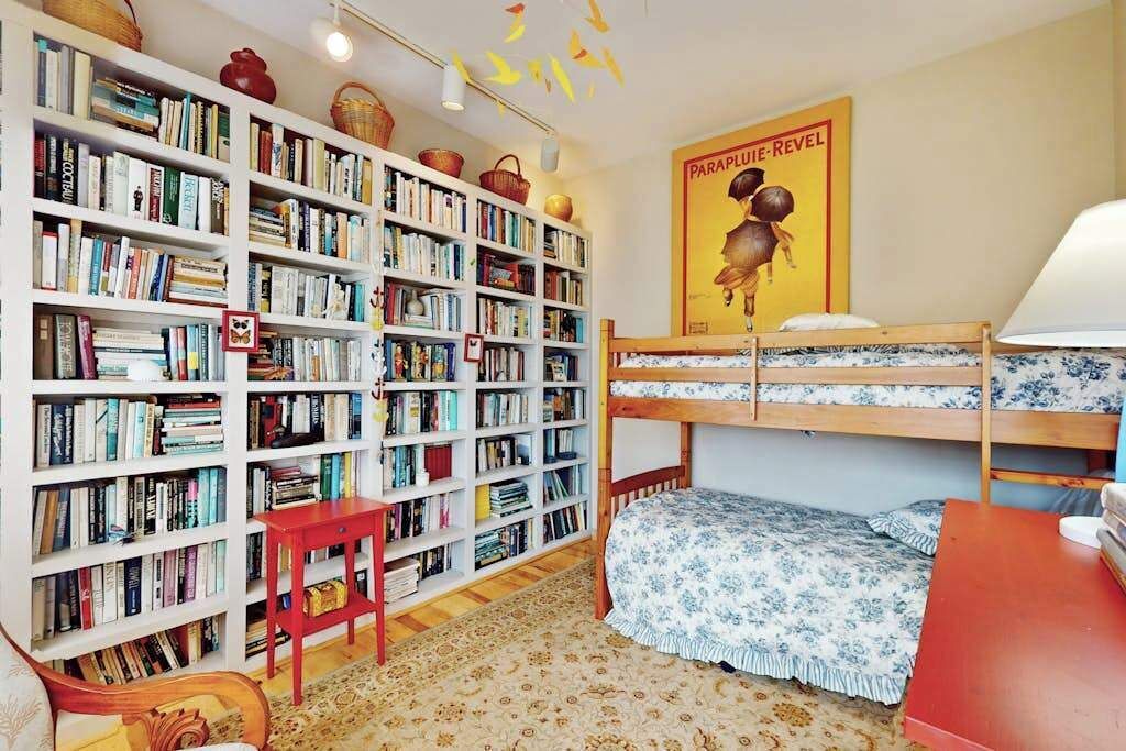 Una habitación con una amplia estantería, dos literas, una mesita pequeña y un cartel en la pared.