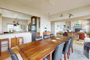 Amplia sala de estar con una gran mesa de comedor de madera, asientos cómodos, una zona de cocina y una chimenea.