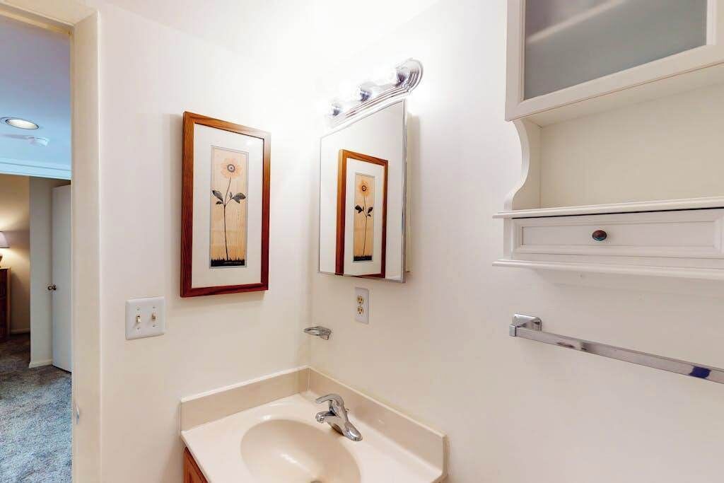 Une salle de bain avec un lavabo, un miroir et une œuvre d’art encadrée accrochée au mur.