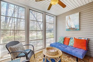A room with large windows, a ceiling fan, a blue sofa with colorful cushions, and a wicker chair. - Sea Colony Tennis townhouse with sauna, gym, & basketball court (Bethany Beach)