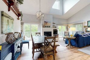 A spacious living area with a dining table, chairs, a sofa, a fireplace, and a large window. - Sea Colony Tennis 2nd-floor condo basketball court & sauna (Bethany Beach)
