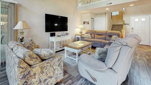 Ein Wohnzimmer mit Flachbildfernseher, gemusterten Sofas, einem Couchtisch und einer Treppe, die zu einer oberen Ebene führt.