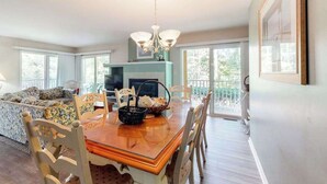 A dining area with a wooden table, chairs, a chandelier, and a sofa with a view to the outside. - 1st-floor Sea Colony Tennis condo with sauna & pool (Bethany Beach)