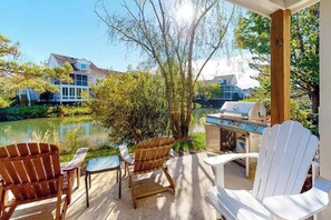 An outdoor patio with Adirondack chairs, a grill, and a view of a lake and houses. - Sea Colony Tennis Townhouse w/ Pools, Tennis, Pickleball & Gym (Bethany Beach)