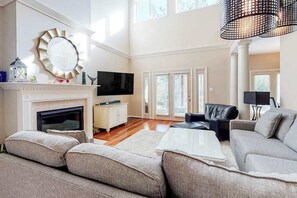 A spacious living room with a fireplace, a television, and a large window. - Sea Colony Tennis Townhouse w/ Pools, Tennis, Pickleball & Gym (Bethany Beach)