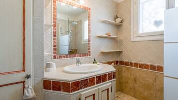A bathroom with a sink, mirror, shower, and tiled walls.
