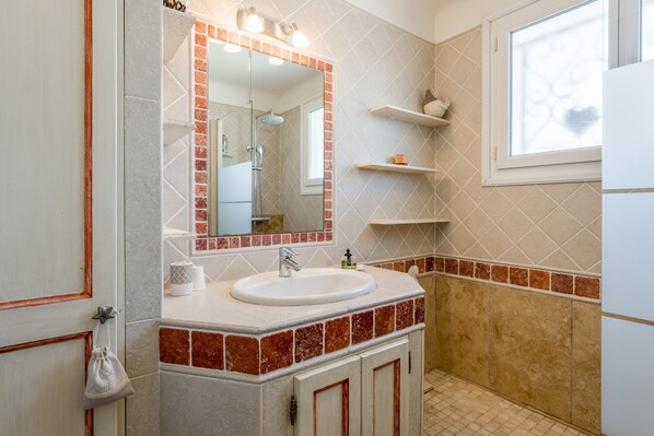 A bathroom with a sink, mirror, shower, and tiled walls.