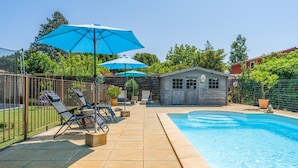 A backyard with a swimming pool, lounge chairs, and umbrellas.