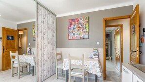 A dining area with a table and chairs, a colorful artwork on the wall, and a wooden door.