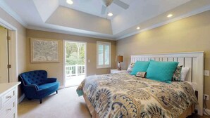 Une chambre avec un grand lit, un fauteuil bleu, un ventilateur de plafond et une vue sur l’extérieur.