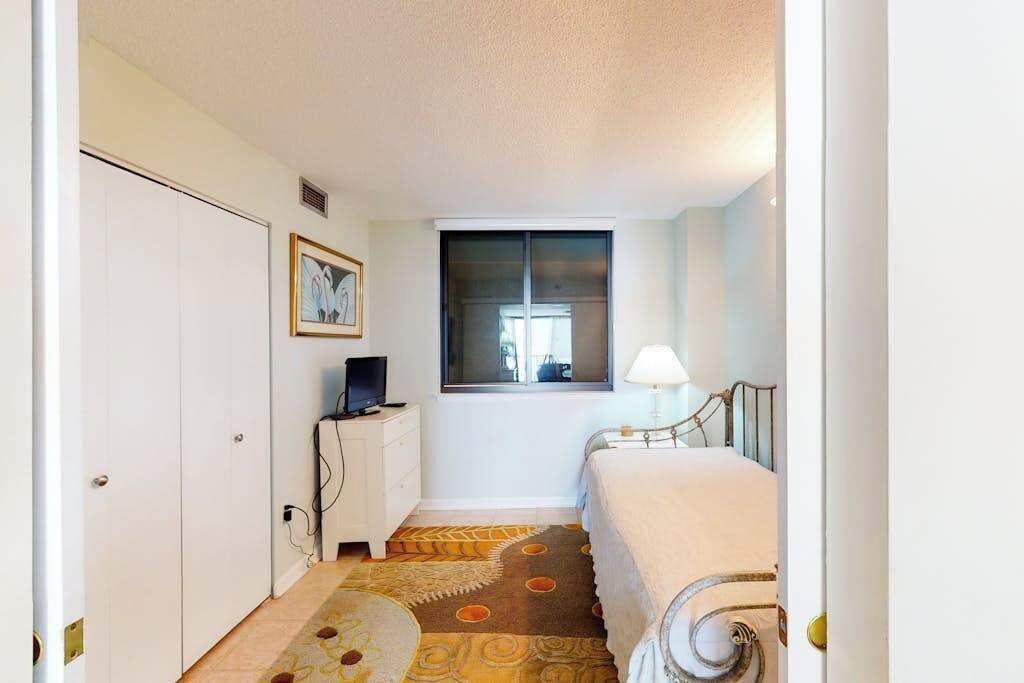A bedroom with a bed, a desk with a computer, a window, and a door.