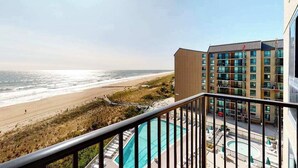 A balcony with a view of the beach and ocean, a pool, and a building with multiple floors and windows. - Sea Colony Ocean 7th floor condo w/ gym, balcony, and tennis court (Bethany Beach)