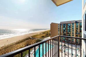 Ein Balkon mit Blick auf Strand und Meer, ein Pool und ein Mehrstöckiger Gebäudebau mit Fenstern.